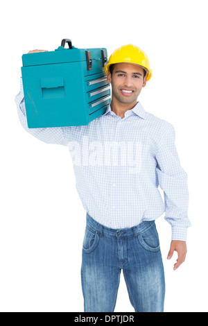 Portrait of a smiling handyman in hard hat transportant une boîte à outils Banque D'Images