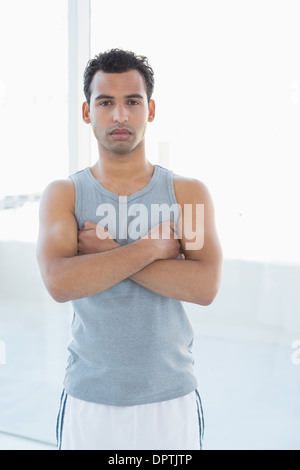 Fit young man standing with arms crossed in fitness studio Banque D'Images