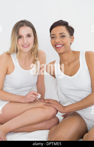 Pretty woman painting friends nails on bed Banque D'Images