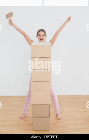 Femme avec pile de boîtes et le pinceau dans une nouvelle maison Banque D'Images