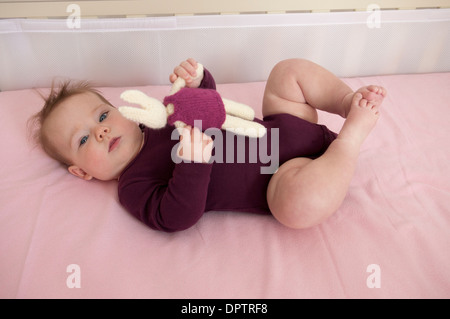 Baby Girl couché dans son lit et jouer avec un jouet mou Banque D'Images