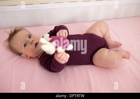 Baby Girl couché dans son lit et jouer avec un jouet mou Banque D'Images