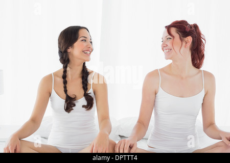 Deux smiling women in white tops sitting on bed Banque D'Images
