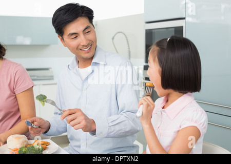 Père petite fille regardant manger avec une fourchette dans la cuisine