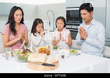 Famille de quatre disant grace avant repas dans la cuisine Banque D'Images