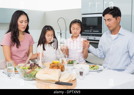 Famille de quatre disant grace avant repas dans la cuisine Banque D'Images