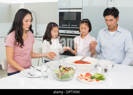 Famille de quatre disant grace avant repas dans la cuisine Banque D'Images