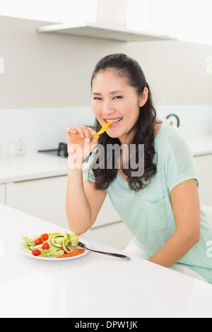 Portrait of a young woman eating salad in kitchen Banque D'Images