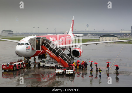 Les passagers d'Air Asia airlines vol avec escalier dans la pluie, avec un parapluie rouge fourni par la compagnie aérienne Banque D'Images