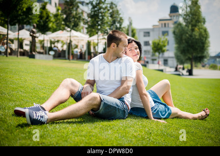 Jeune couple assis sur l'herbe, se penchant avec dos et smiling over shoulder Banque D'Images