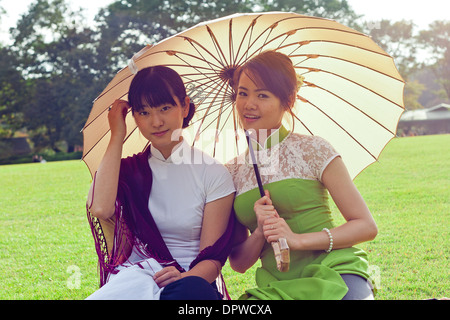 Pour les jeunes femmes des parasols en robe traditionnelle vietnamienne à genoux smiling at camera Banque D'Images