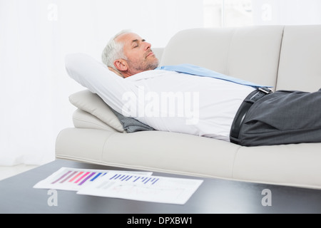 Businessman sleeping on sofa avec les graphiques sur le tableau dans la salle de séjour Banque D'Images