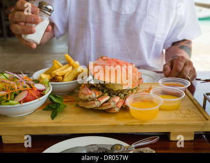 Un homme sur le point de manger un repas d'un crabe entier fraîchement cuit, pommes frites et salade avec du beurre fondu et les trempettes. Rarotonga, îles Cook. Banque D'Images