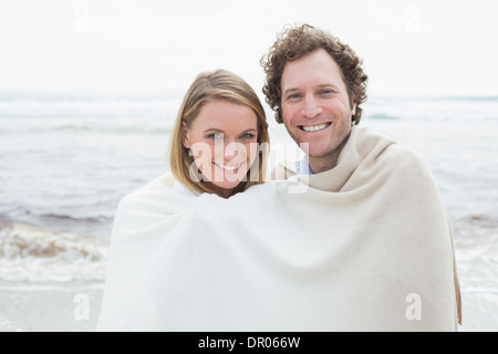 Smiling couple wrapped in blanket at beach Banque D'Images