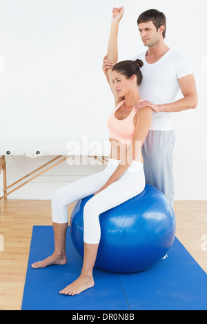 Femme sur le yoga ball tout en travaillant avec le thérapeute physique Banque D'Images
