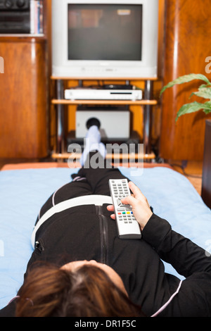 Femme d'âge moyen avec télécommande en regardant la télé à la maison. Profondeur de champ avec l'accent sur le contrôle à distance. Banque D'Images