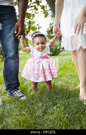 Parents helping daughter walk in park Banque D'Images