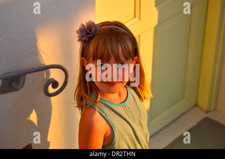 Portrait of little girl smiling blonde en vacances à la recherche jusqu'à la caméra en tant qu'elle est baignée de soleil à Santorin Grèce Banque D'Images