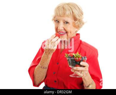 Monter healthy senior woman biting dans une fraise et tenait un bol de fruits des champs. Banque D'Images