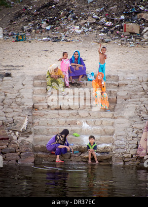 Les femmes et les enfants assis sur les mesures sur la rive du Nil, l'Egypte, avec une décharge derrière eux. Banque D'Images