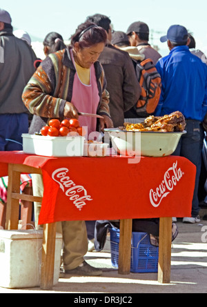 Femme autochtone préparer les repas de tomates et de viande rôtie au décrochage routière avec coca cola sign in ville d'Oruro en Bolivie Banque D'Images