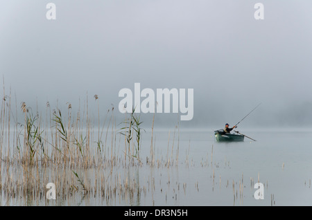 Un homme pêche dans la brume, à partir d'un bateau sur le lac de Clairvaux, le Jura, France. Banque D'Images