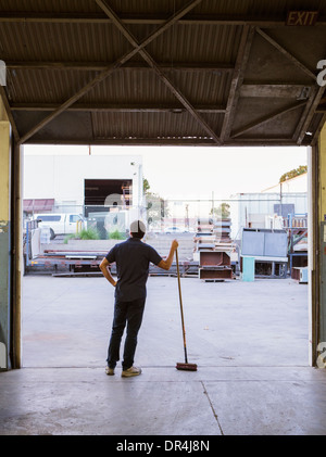 Worker holding broom in warehouse Banque D'Images