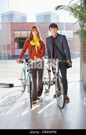 Les gens d'affaires wheeling bicyclettes dans office Banque D'Images