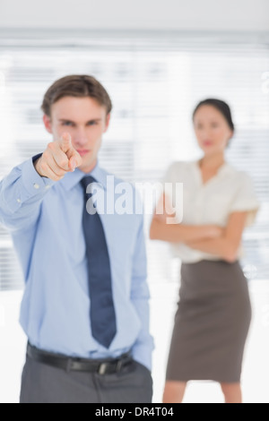 Businessman pointing towards camera with woman in office Banque D'Images