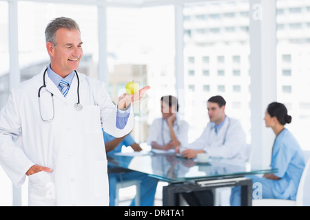 Doctor holding apple avec le groupe autour de la table à l'hôpital Banque D'Images