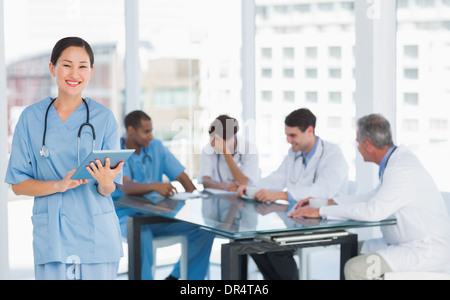 Chirurgien using digital tablet with group around table in hospital Banque D'Images