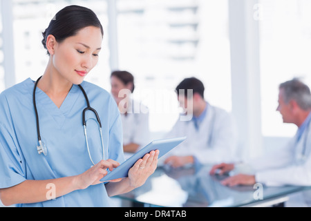 Chirurgien using digital tablet with group around table in hospital Banque D'Images