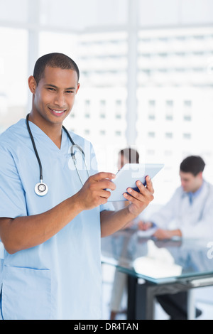 Chirurgien using digital tablet with group around table in hospital Banque D'Images