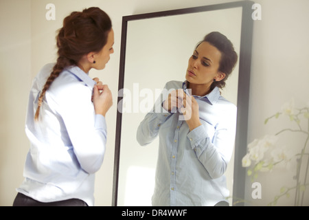 Attractive young woman in front of mirror de boutonner sa chemise. Belle femme de race blanche s'habiller pour le bureau. Banque D'Images