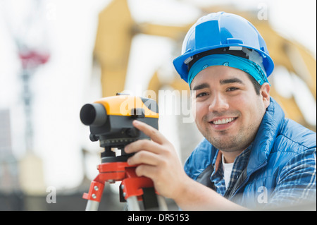 Ingénieur de course mixte à l'aide d'un théodolite at construction site Banque D'Images