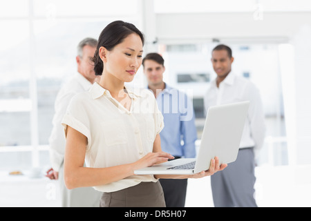 Pretty asian businesswoman using laptop avec l'équipe derrière elle Banque D'Images