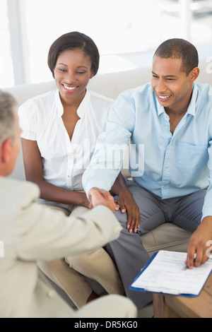 Young smiling couple shaking hands with salesman sur canapé Banque D'Images