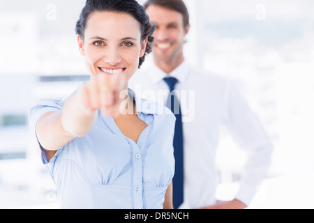 Happy woman pointing at camera with colleague in background Banque D'Images