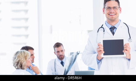 Doctor holding digital tablet with colleagues in meeting Banque D'Images