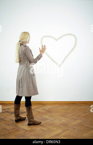 Jeune femme à la recherche de forme de coeur sur le mur, Munich, Bavière, Allemagne Banque D'Images