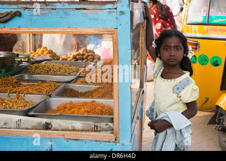 Jeune indienne debout à côté d'une douce et fried street kitchen à un marché indien. Puttaparthi, Andhra Pradesh, Inde Banque D'Images