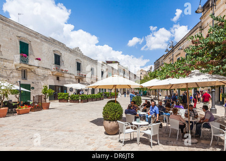 Les touristes profiter de cafés en terrasse sous les parasols dans Via Pascoli, Matera, Basilicate, Italie sur une journée ensoleillée sous un ciel bleu Banque D'Images