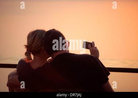 Europe Grèce cyclades sikinos un couple de prendre une photo d'eux-mêmes avec le coucher du soleil Banque D'Images