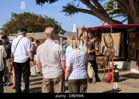 Les touristes à regarder un artiste au travail peinture photos dans l'état occupé dimanche street market dans Teguise, Lanzarote, îles Canaries, Espagne Banque D'Images