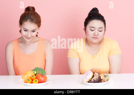 Une fine et grassouillet femme assise à table avec des aliments différents à l'avant Banque D'Images