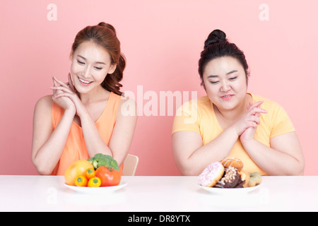 Une fine et grassouillet femme assise à table avec des aliments différents à l'avant Banque D'Images