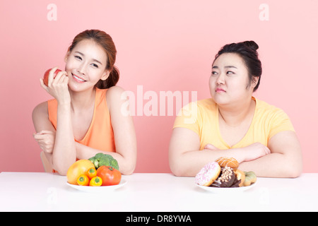 Une fine et grassouillet femme assise à table avec des aliments différents à l'avant Banque D'Images