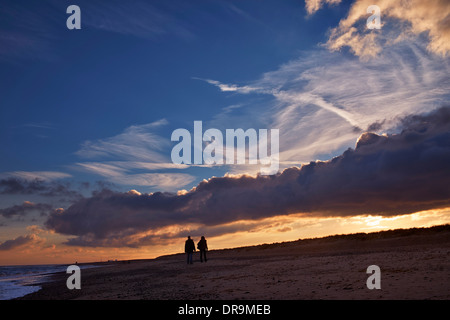 Couple en train de marcher le long de la plage au crépuscule. Southwold, Suffolk, Angleterre. Banque D'Images