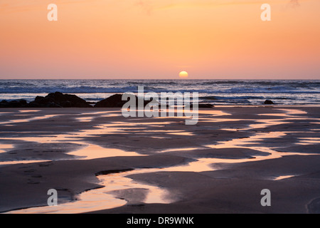 L'orange vif soleil qui reflète dans l'eau de ruisseaux sinueux sur Porthtowan Beach à Cornwall, UK Banque D'Images