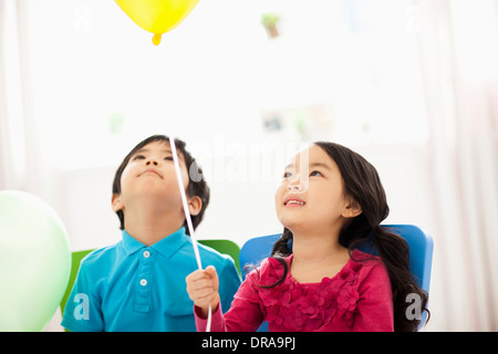 Les enfants assis à côté de l'autre holding balloons Banque D'Images